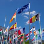Low angle view of European Union flags on flagpoles against a blue sky, symbolizing unity.